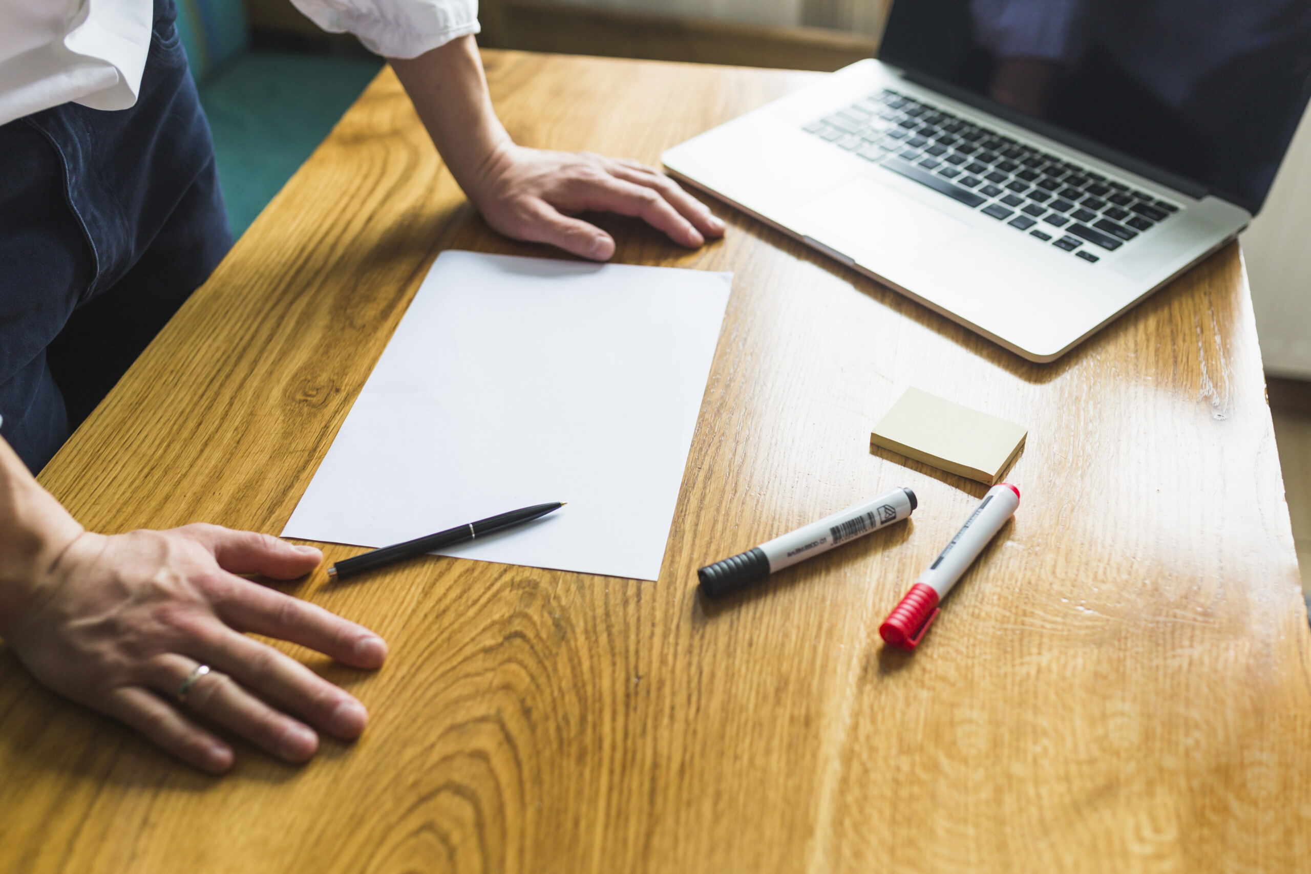 businessperson-s-hand-with-blank-white-paper-wooden-desk